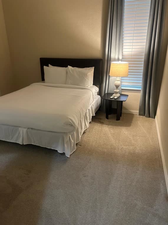Bedroom with a made bed, white linens and a bedside lamp.