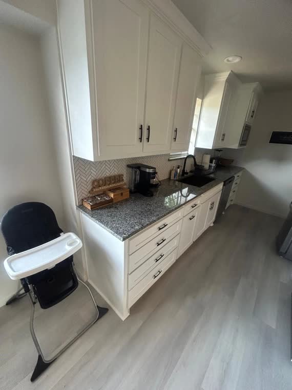 Kitchenette with white cabinets, granite counter and a high chair.